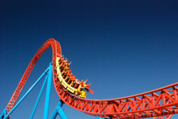 Red rollercoaster with yellow cars descending containing people with arms raised