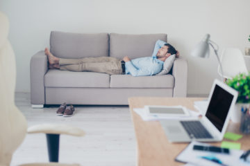 Man lying asleep an lounge with office desk in foreground