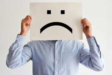 Man in light blue long sleeve shirt holding a frowny in front of his face